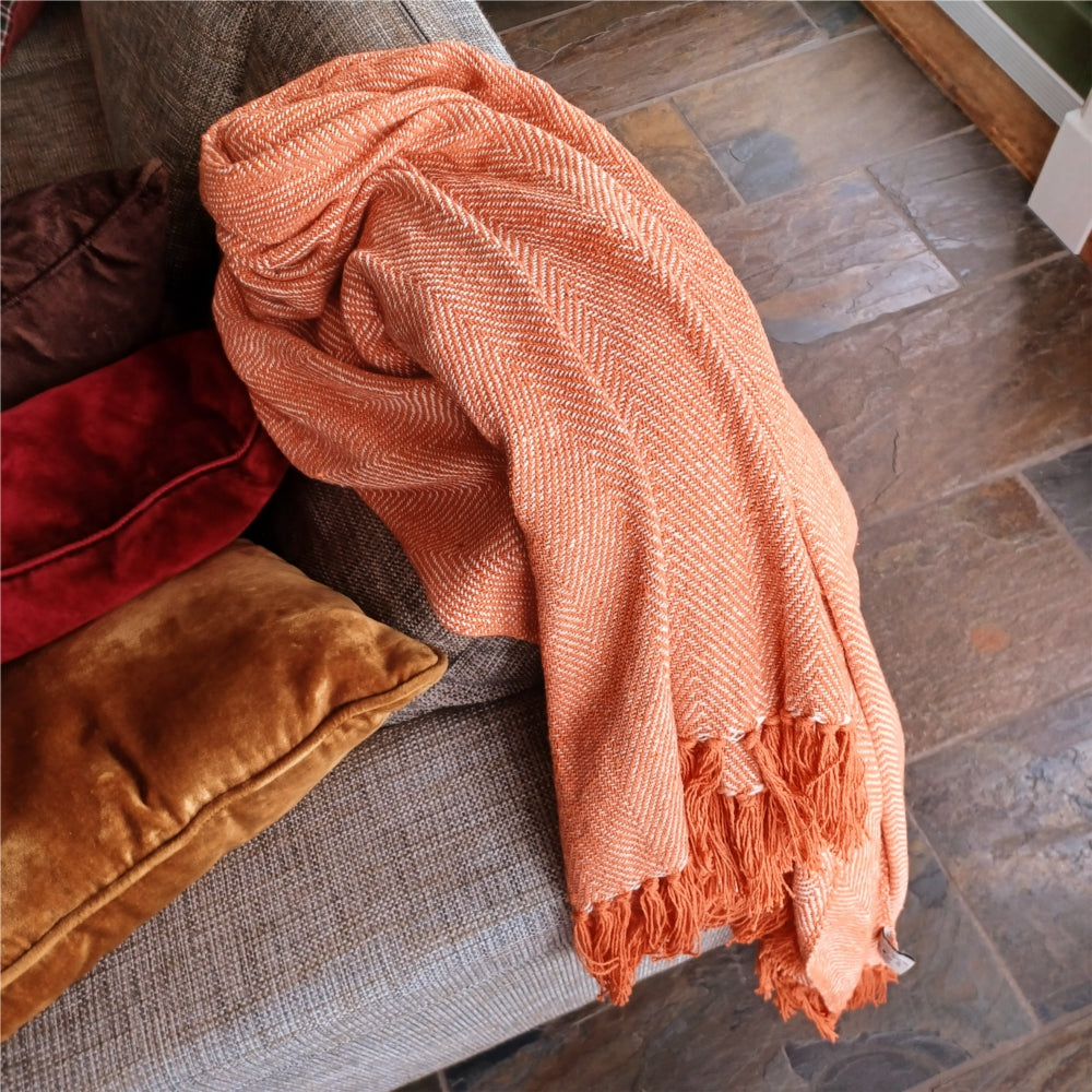 Orange fiskbenspläd i bomull placerad över säng i sommarstuga eller fritidshus