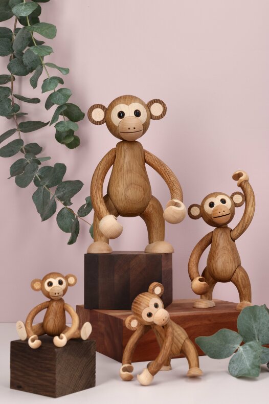 Fyra träapor i olika storlekar arrangerade på träblock med gröna blad
