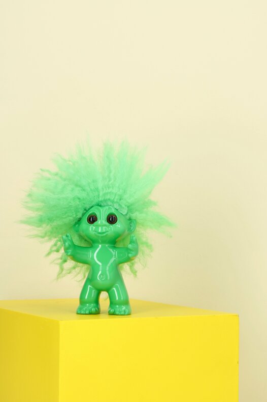 Litet lyckotroll i grönt placerat på gul yta i ett ljust lantkök