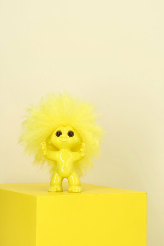 Lyckotroll i gult stående på en matchande gul yta