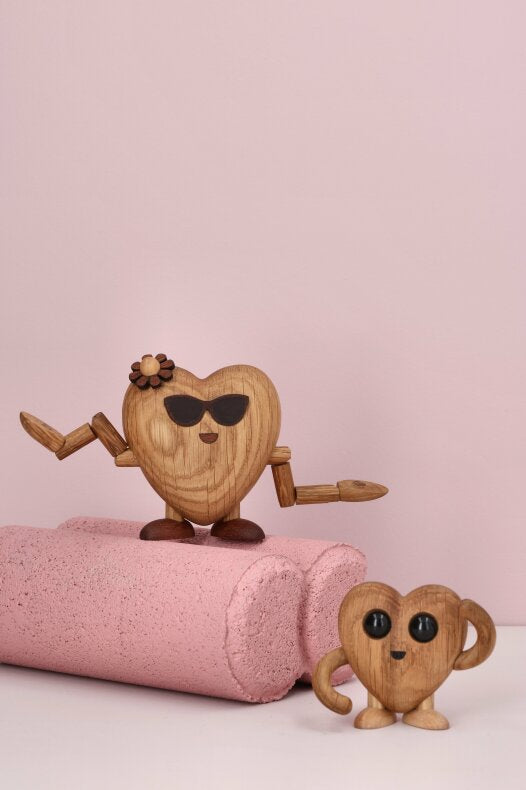 Två hjärtformade trädekorationer i olika storlekar på rosa bakgrund