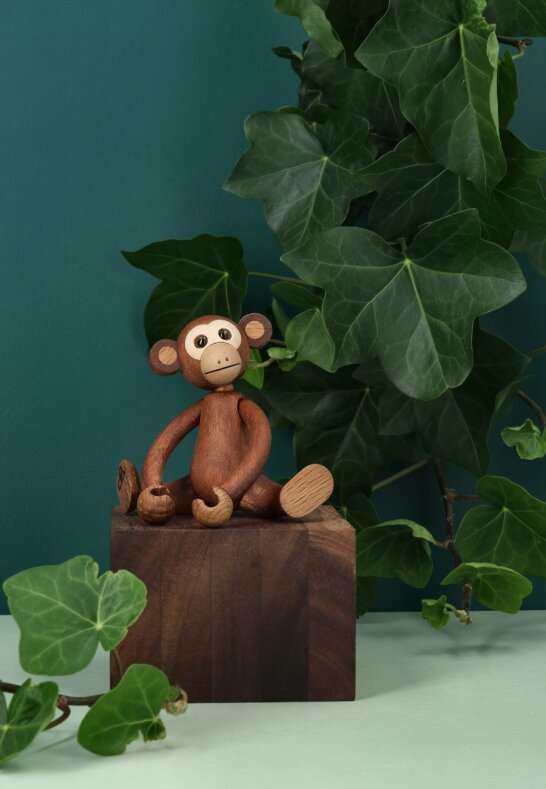 Trädekoration apa sittandes på ett mörkt träblock intill gröna murgrönsblad