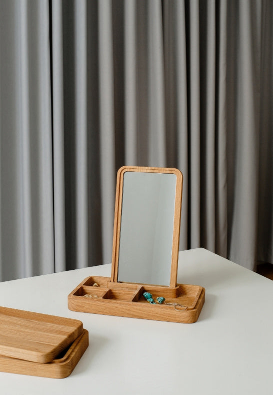 Smyckeskrin i ek med smycken och spegel på vitt bord i ett ljust rum