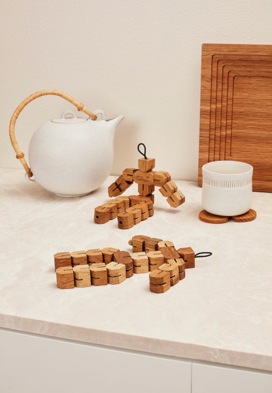 Två grytunderlägg i ek bredvid tekanna och kopp i lantkök