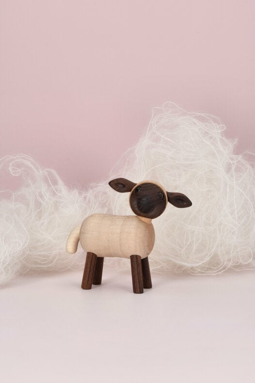 Liten lammfigur i FSC-certifierat trä placerad i mjuk vit ull