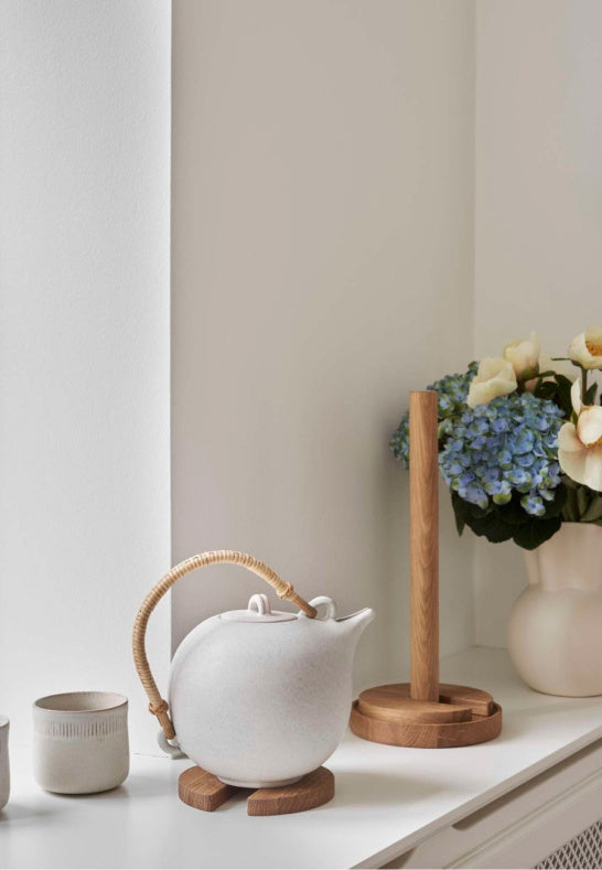 Stilren hushållspappershållare i ek intill en vit keramiktekanna i fönstret